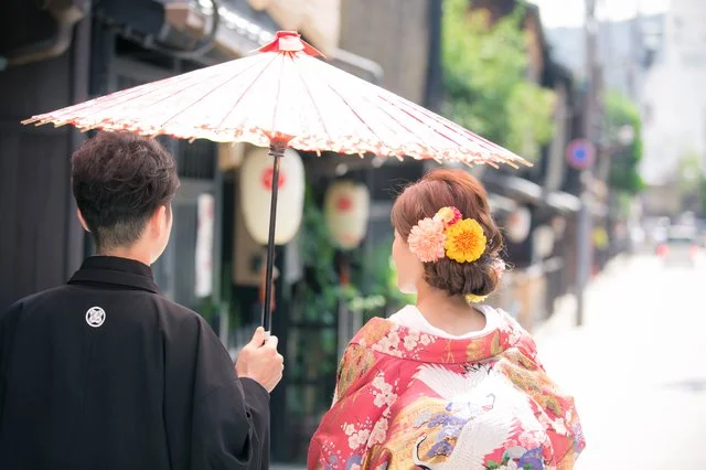 和傘を差して京都の街並みを歩く、袴と着物姿の男女の後ろ姿